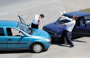 Two nervous arguing businessmen standing in the street by their crashed cars.