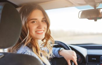 Close up portrait of pleasant looking female with glad positive expression, being satisfied with unforgettable journey by car, sits on driver`s seat, enjoys music. People, driving, transport concept